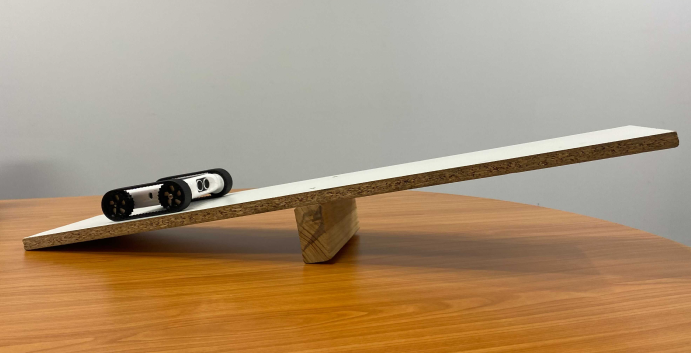 Balance Bot setup, a hard-cover book on a small wooden see-saw
